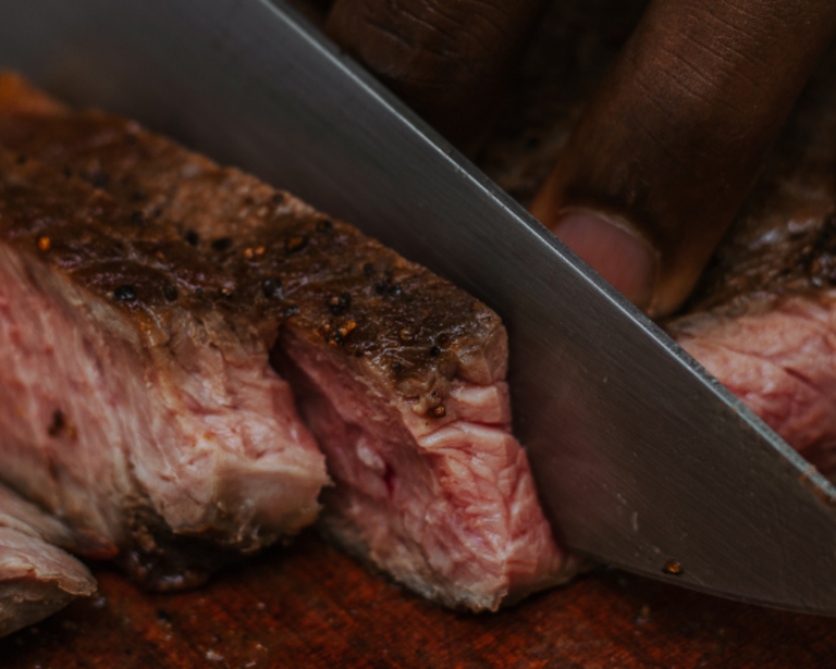 main qui coupe un morceau de bœuf 